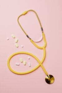 A yellow stethoscope and pills on a pink background highlighting essential vitamins.