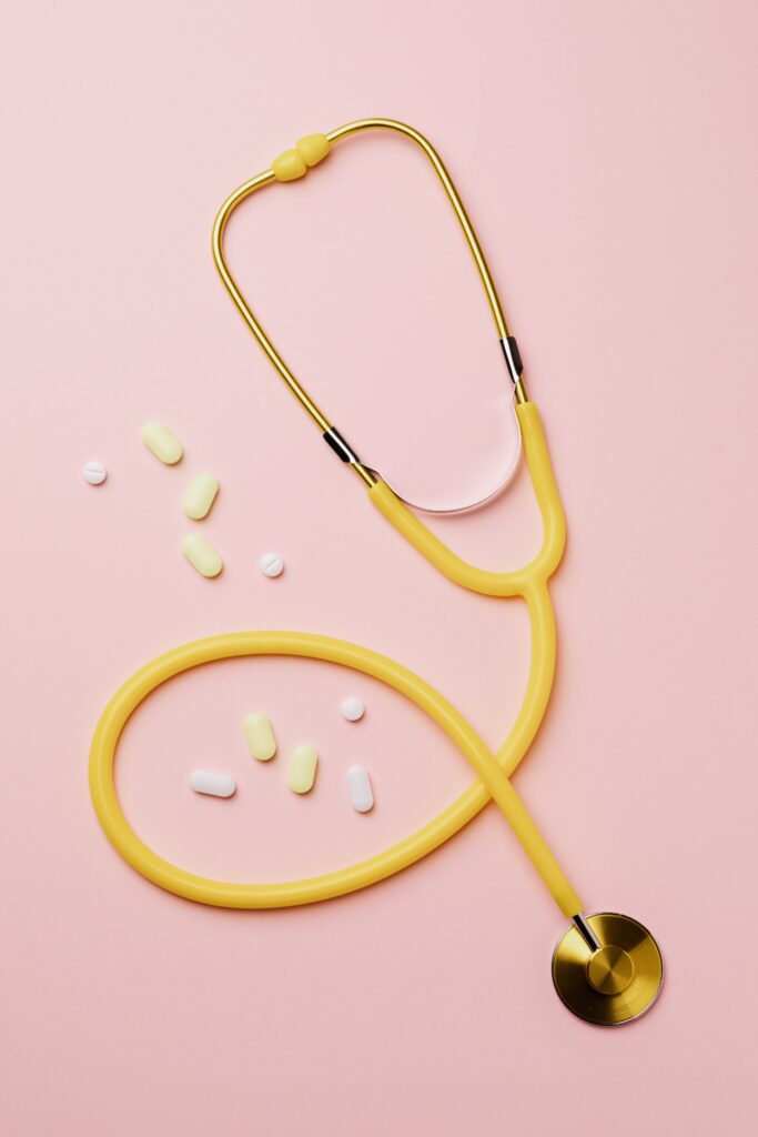 A yellow stethoscope and pills on a pink background highlighting essential vitamins.
