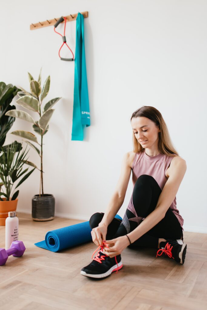 A woman exercising by tying her shoes on the floor in front of a plant.