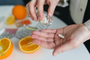 A woman is organizing sports nutrition pills next to oranges in a jar.