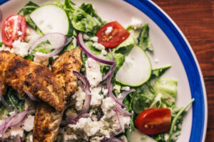 A plate of chicken salad with tomatoes, cucumbers and onions.
